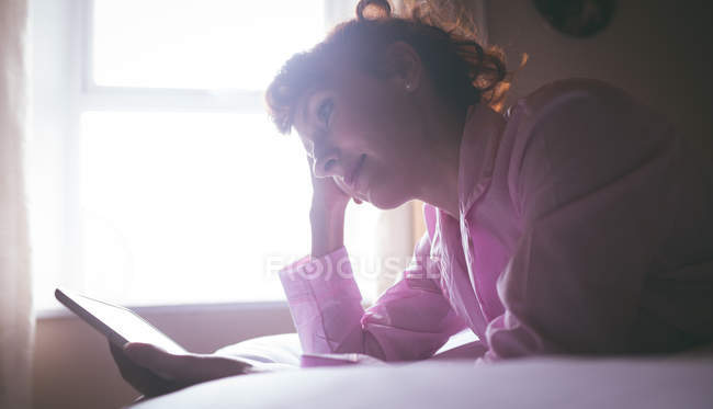 Woman using digital tablet while lying on bed in bedroom at home — Stock Photo