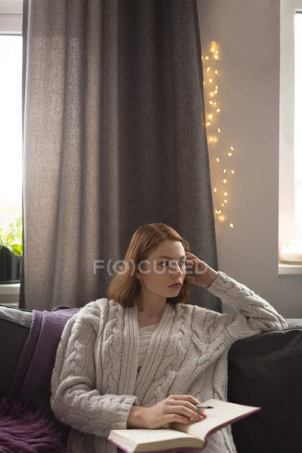 Thoughtful woman writing on a diary in living room at home — Stock Photo