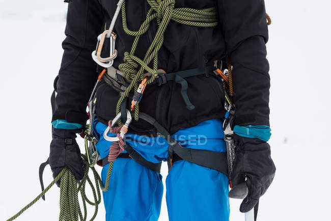 Male mountaineer standing with rope and harness on a snowy region — Stock Photo