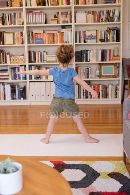 Vue arrière de la petite fille effectuant des exercices d'étirement dans le salon à la maison — Photo de stock