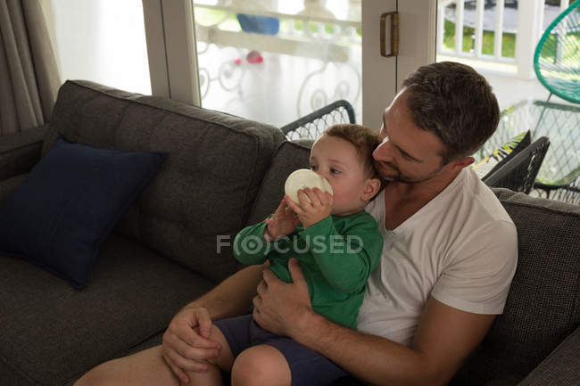 Pai olhando para seu filho bebendo leite na sala de estar em casa — Fotografia de Stock