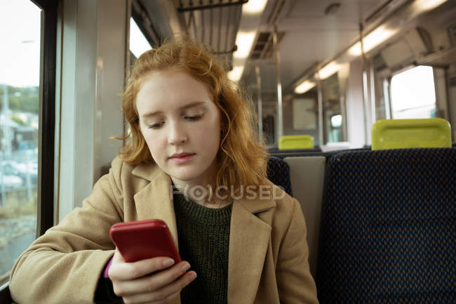 Рыжие волосы молодая женщина использует свой мобильный телефон в поезде — стоковое фото