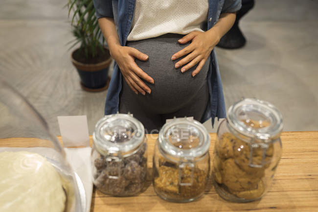 Pregnant businesswoman looking at sweet food in cafeteria at office — Stock Photo