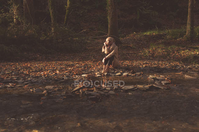 Mujer pensativa sentada en el bosque durante el otoño - foto de stock
