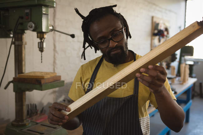 Carpenter looking at wooden plank in workshop — Stock Photo