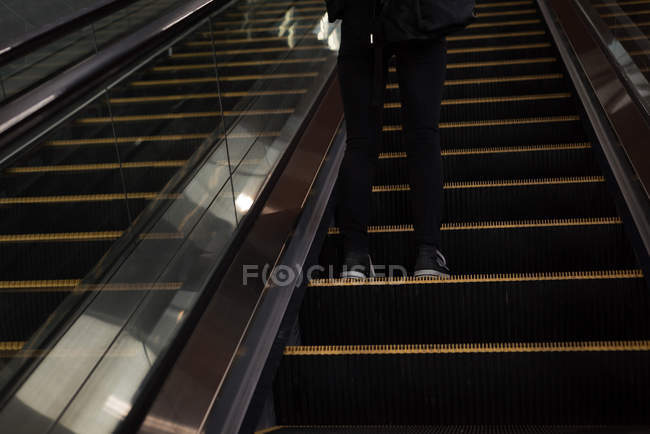 Sección baja de la mujer de pie moviéndose desde una escalera mecánica en la estación - foto de stock