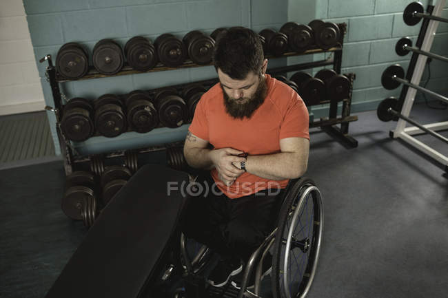 Hombre discapacitado viendo el tiempo en el reloj de pulsera en el gimnasio - foto de stock