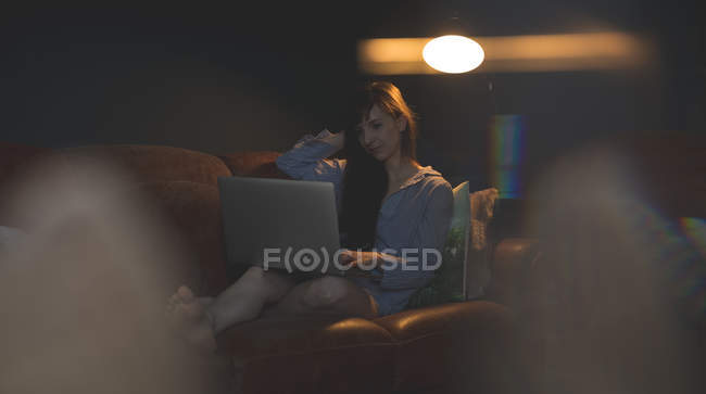 Woman using laptop on sofa in living room at home — Stock Photo