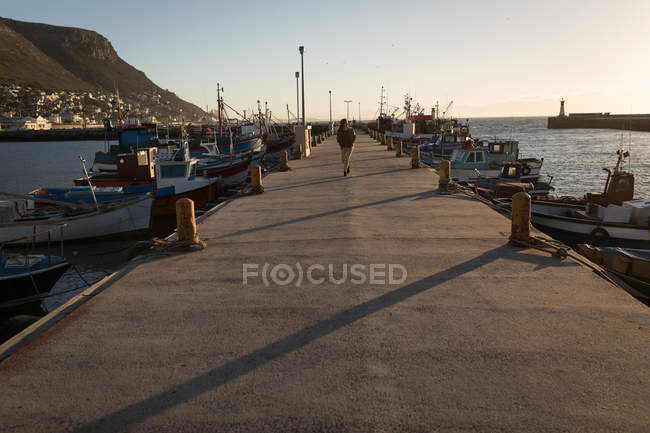 Woman walking on dock near moored boats in sunlight — Stock Photo