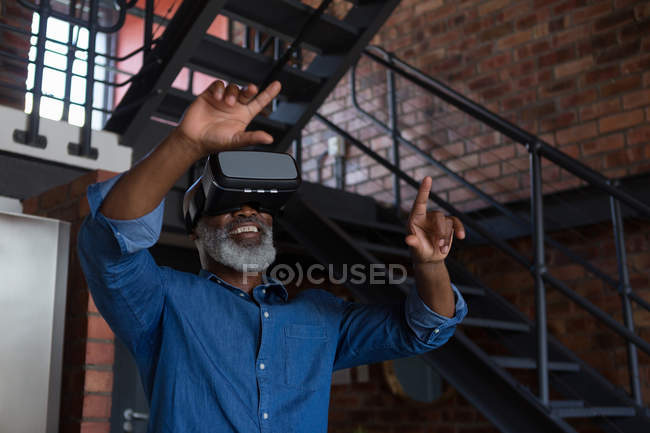 Улыбающийся пожилой человек с помощью гарнитуры виртуальной реальности дома — стоковое фото