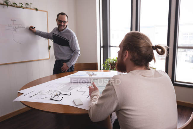 Männliche Führungskraft diskutiert Diagramm auf Whiteboard mit Mitarbeiter im Büro — Stockfoto