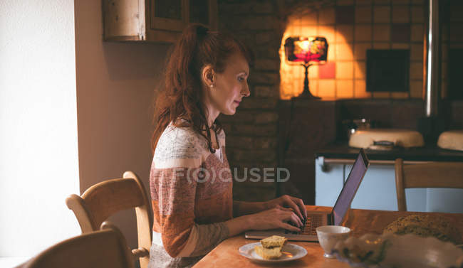 Woman using laptop while having breakfast at home — Stock Photo