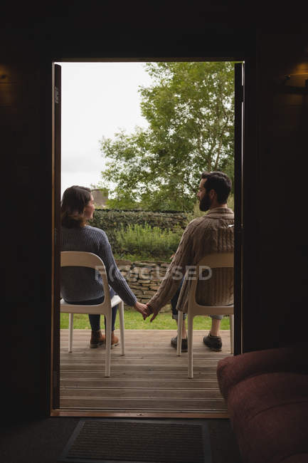 Вид сзади пары, держащейся за руки, сидящей на стульях — стоковое фото