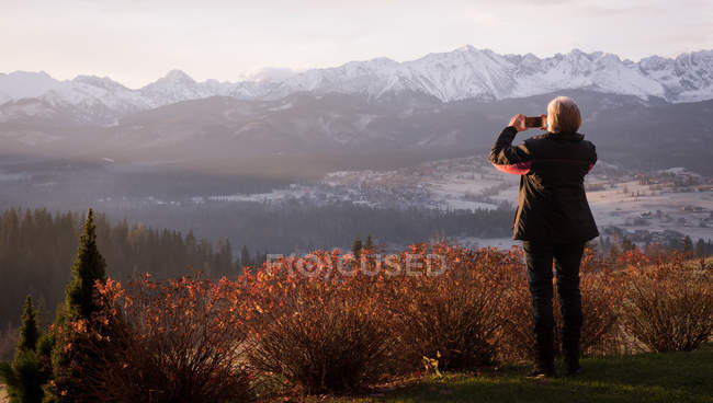 Visão traseira da mulher tirando foto com telefone celular durante o inverno — Fotografia de Stock
