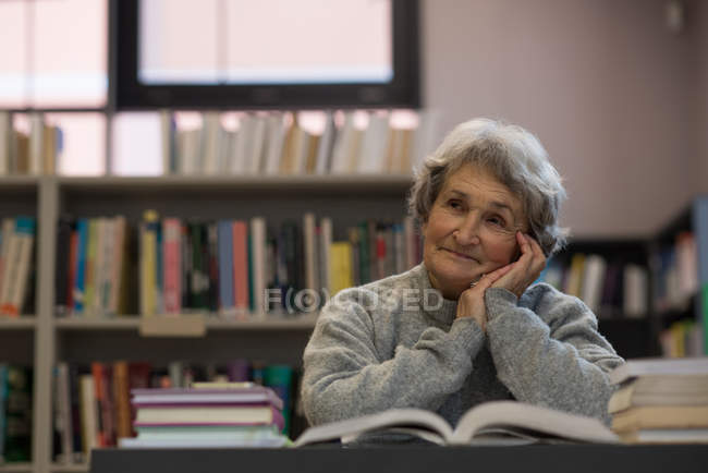 Nachdenkliche Seniorin lächelt in Bibliothek — Stockfoto