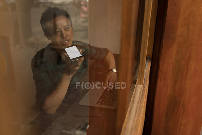Businessman talking on mobile phone in cafe behind window glass — Stock Photo