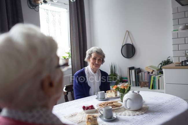 Старші друзі взаємодіють один з одним, снідаючи вдома — стокове фото