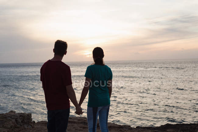 Silueta de pareja cogida de la mano en la playa al atardecer - foto de stock