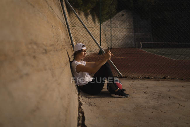 Молодая женщина с помощью мобильного телефона на баскетбольной площадке — стоковое фото
