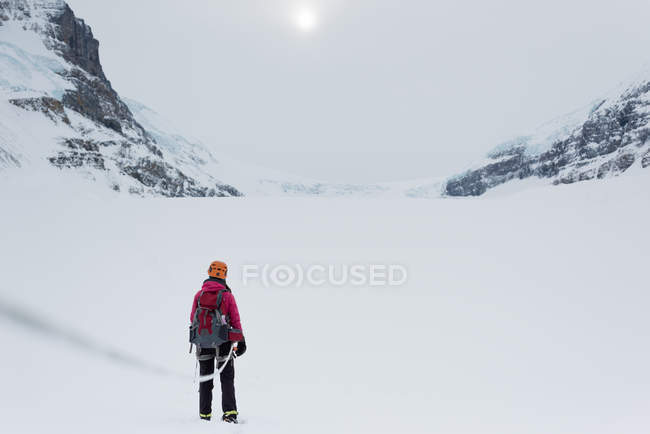 Rear view of female mountaineer standing with backpack on a now covered mountain during winter — Stock Photo