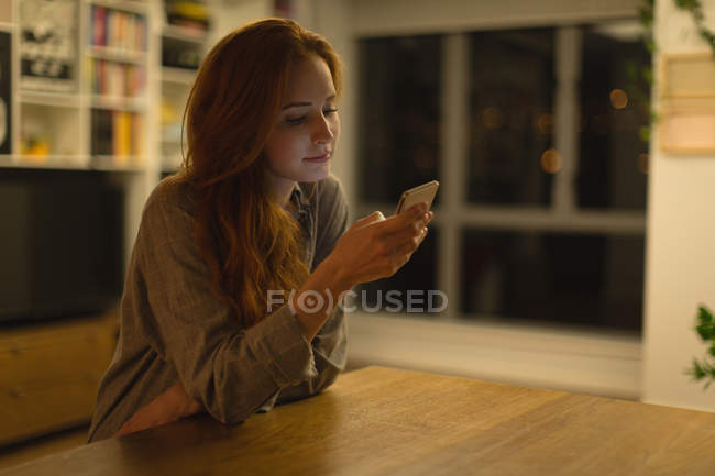 Jovem mulher usando telefone celular em casa — Fotografia de Stock