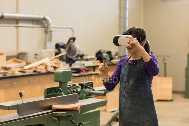 Carpinteiro feminino usando fone de ouvido de realidade virtual na oficina — Fotografia de Stock