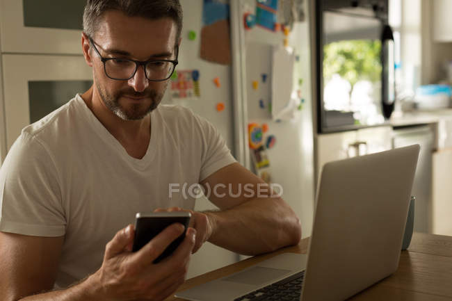 Людина використовує мобільний телефон під час роботи на ноутбуці вдома — стокове фото