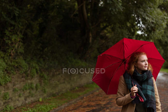 Mujer joven de pie con paraguas en el parque - foto de stock