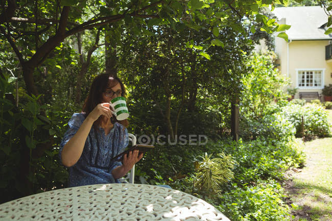Mulher atenciosa tomando café enquanto usa tablet digital no jardim — Fotografia de Stock