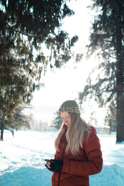 Женщина в зимней одежде с помощью мобильного телефона в солнечный день — стоковое фото