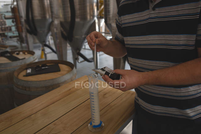 Sección media del trabajador que comprueba la calidad de la ginebra en fábrica - foto de stock