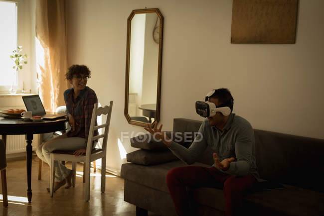 Жінка, дивлячись на людину при використанні віртуальної реальності гарнітуру у вітальні — стокове фото