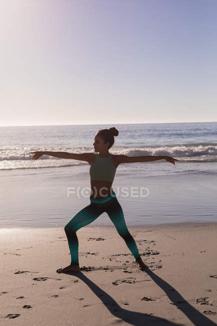 Вмістити жінку, що виконує розтягування вправи на пляжі в сутінках . — стокове фото