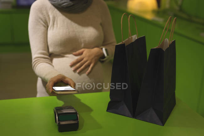 Вагітна жінка робить оплату через мобільний телефон в магазині — стокове фото