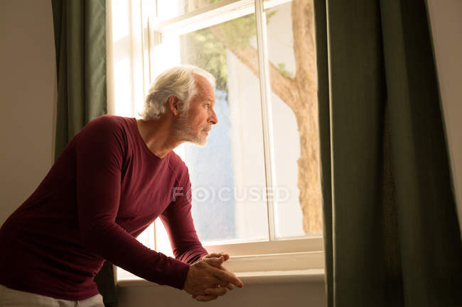 Продуманий старший чоловік дивиться крізь вікно вдома — стокове фото