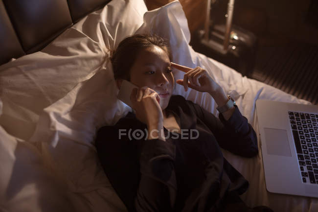 Woman talking on mobile phone wile relaxing on bed — Stock Photo
