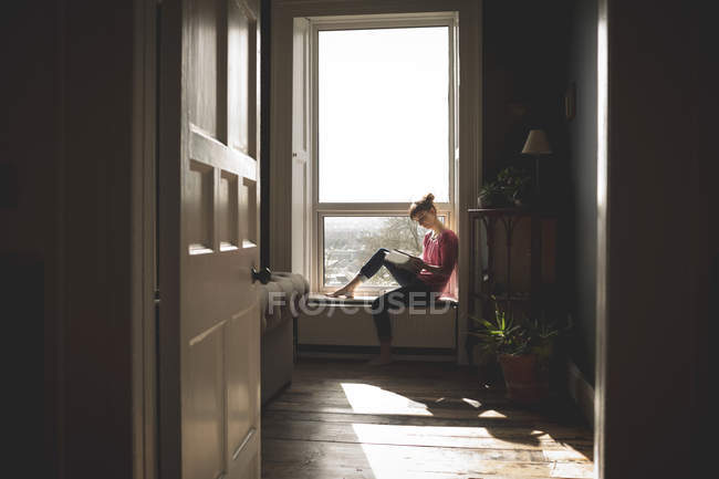 Жінка читає книгу на підвіконні вдома — стокове фото