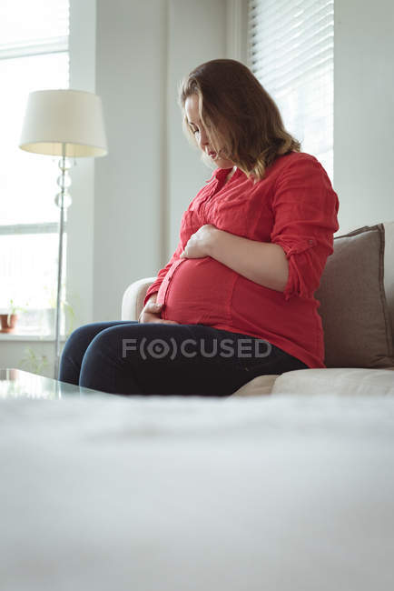 Mujer embarazada mirando hacia abajo hacia su vientre y sosteniéndolo - foto de stock