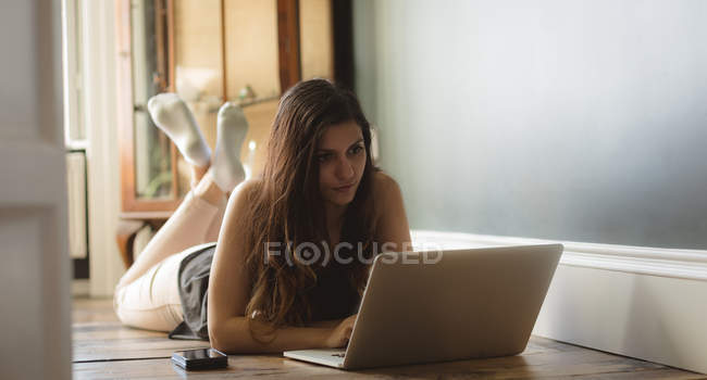 Frau benutzt Laptop, während sie zu Hause auf dem Boden liegt — Stockfoto