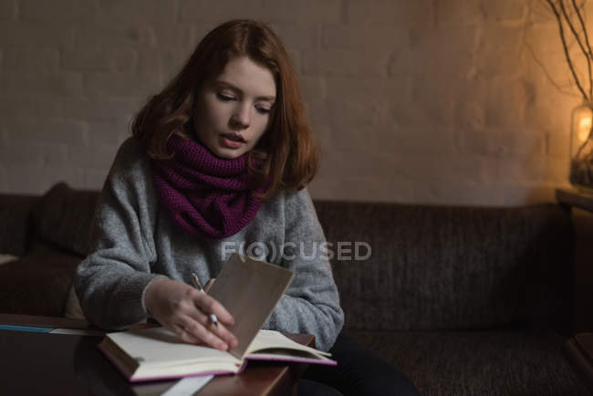Mujer escribiendo nota en el diario en la sala de estar en casa - foto de stock
