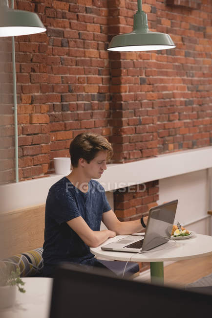 Мужчина использует ноутбук во время завтрака в офисной столовой — стоковое фото