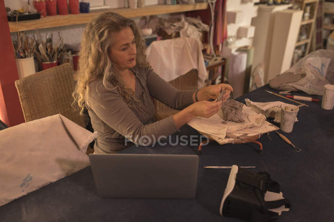 Töpferin schaut auf Laptop, während sie zu Hause Ton formt — Stockfoto