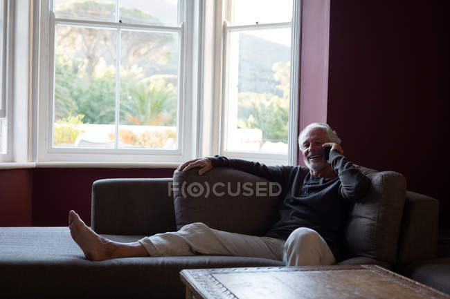 Старший чоловік розмовляє по мобільному телефону у вітальні вдома — стокове фото