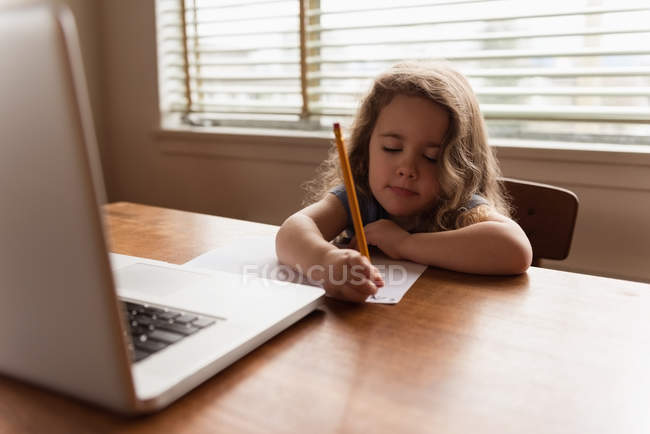 Chica escribiendo con un lápiz en un pedazo de papel en casa - foto de stock