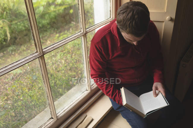 Чоловік читає книгу біля вікна вдома — стокове фото