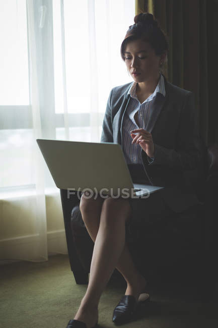 Femme d'affaires utilisant un ordinateur portable tout en étant assis sur un fauteuil dans la chambre d'hôtel — Photo de stock