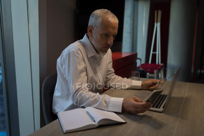 Empresário usando telefone celular enquanto trabalhava em laptop no hotel — Fotografia de Stock