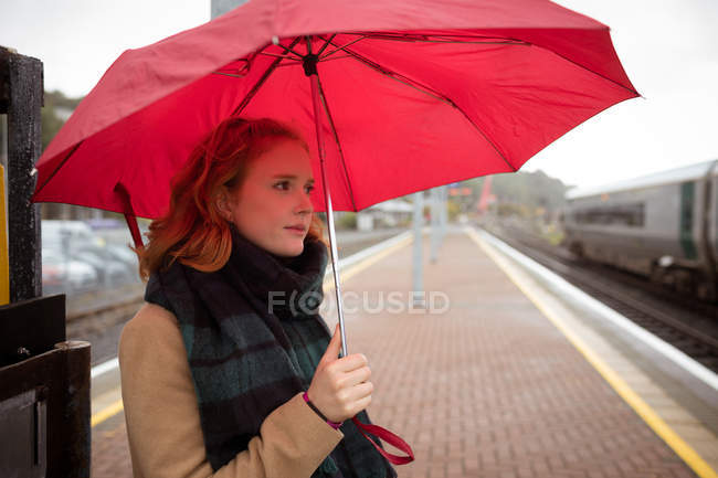 Giovane donna con ombrello in attesa di treno sul binario — Foto stock