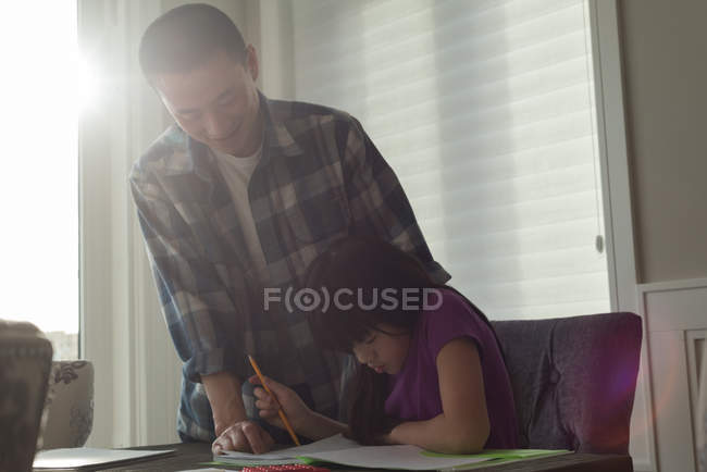 Отец помогает дочери делать домашнее задание дома — стоковое фото