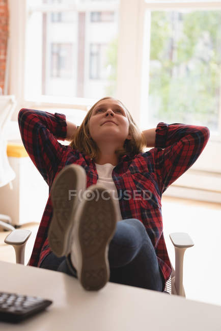 Втомилася жінка-виконавця розслабляється з ногами вгору на столі в офісі — стокове фото